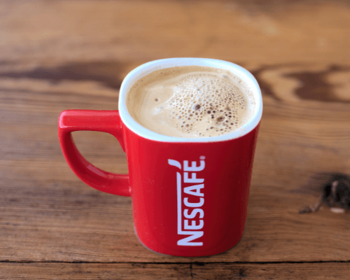 Red mug filled with coffee and "Nescafe" written in white sitting on wooden background - Promotional Products Printing in Brisbane - Call Infinite Print today